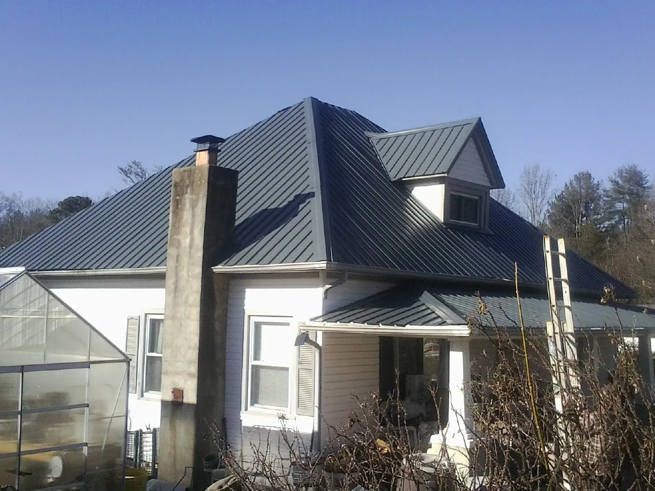 Dark blue standing seam metal roof on a white farmhouse with dormer — Slate & Tile Roof Repair by Roofing Brothers in Pawhuska