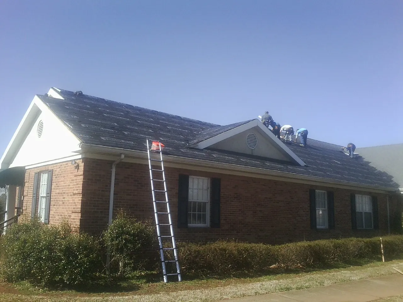 Crew tearing shingles off a brick ranch roof with a ladder set — Metal Roof Repair work by our crew in Pawhuska