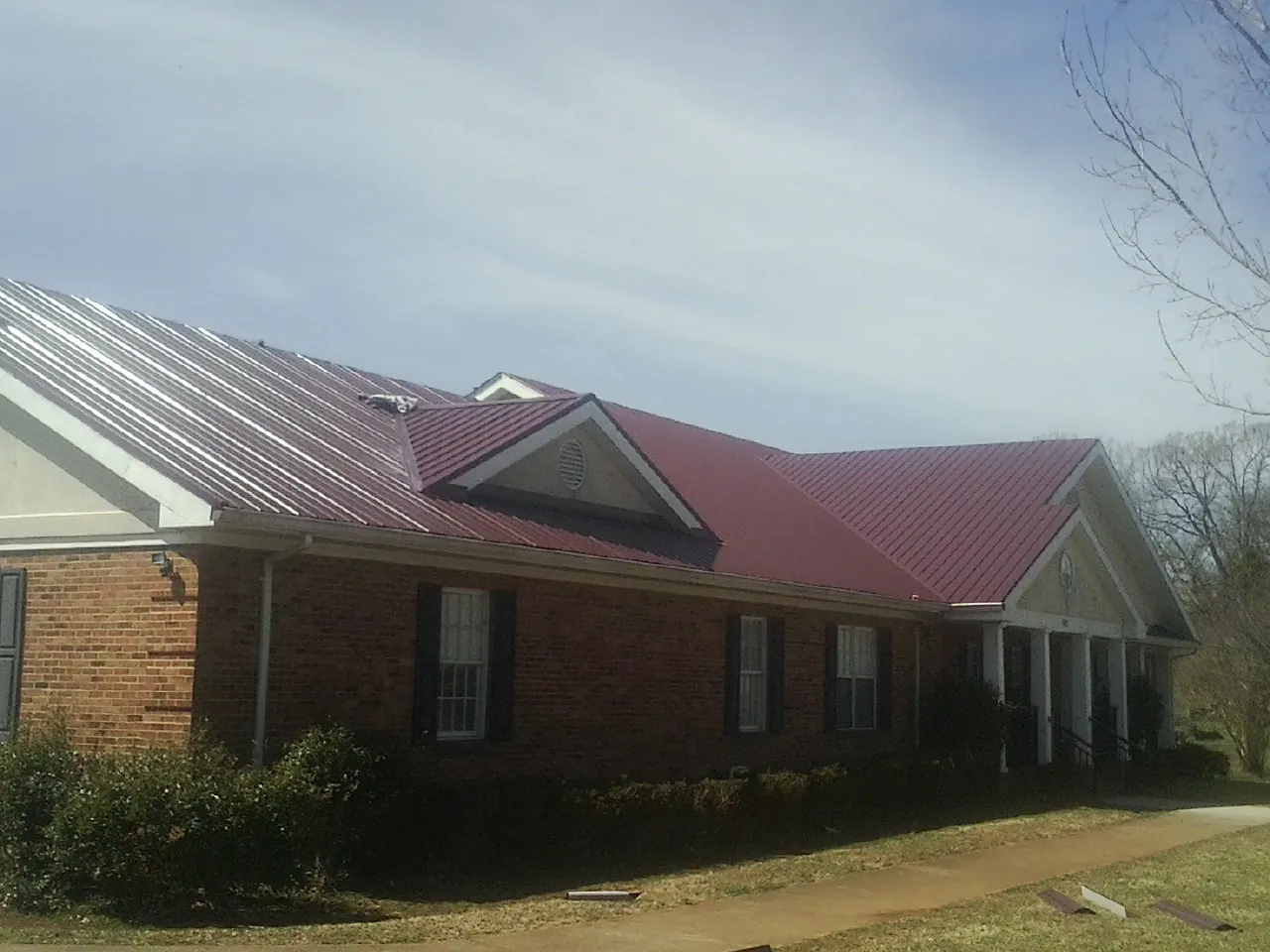Red metal roof with gabled entries on a long brick building, from a Hail Damage Roof Repair job in Pawhuska