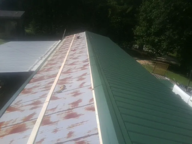Old rusted panels beside newly installed green metal roofing — Wind Damage Roof Repair by Roofing Brothers in Pawhuska