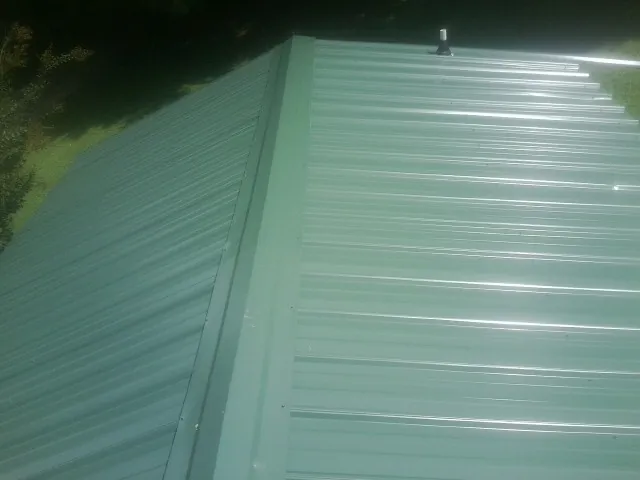 New green metal panels meeting at the ridge of a roof — Flat Roof Repair work by our crew in Pawhuska