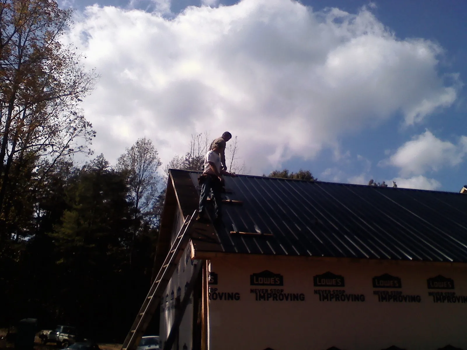 Roofer fastening dark metal panels high against a cloudy sky, from a Roof Inspection job in Pawhuska
