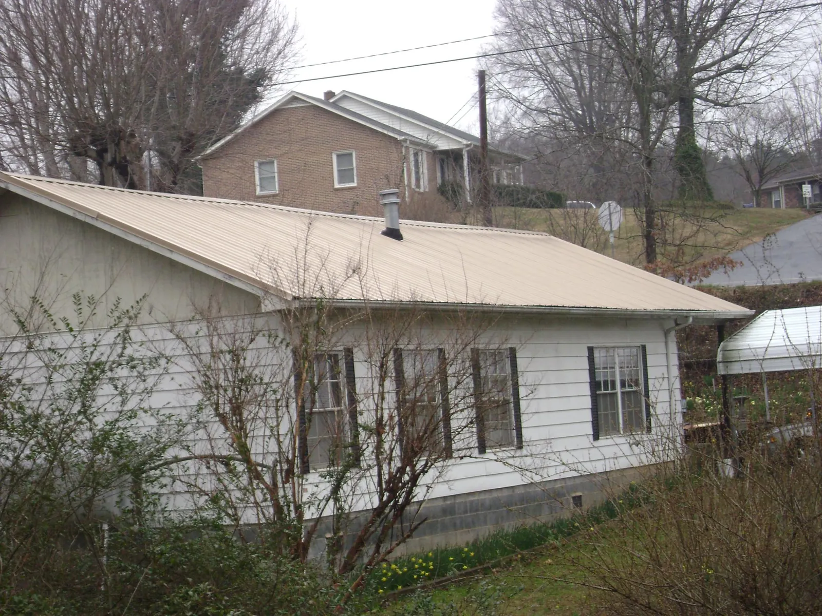 Tan metal roof on a white sided house set into a hillside — Commercial Roofing by Roofing Brothers in Pawhuska