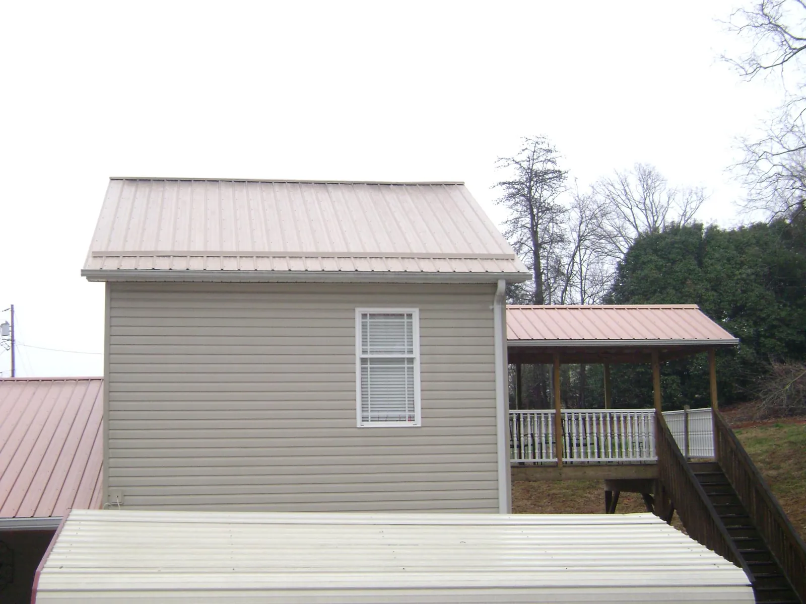 Tan metal roofs on a two story addition and attached porch, from a Roof Replacement job in Pawhuska